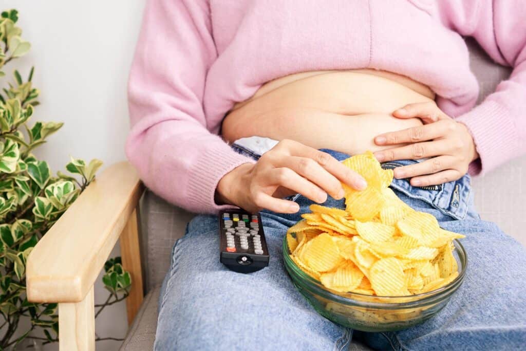 woman sitting on the sofa eating chips and watching TV
