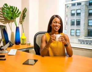 Entreprenuer smiling and holding a cup of coffee at her desk because she used these self care tips