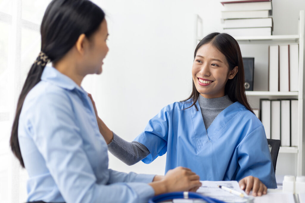 A nurse in scrubs interacts with a patient in a bright, modern clinic, both smiling in a supportive atmosphere.