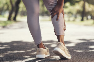woman wearing purple leggings and tan tennis shoes holding leg